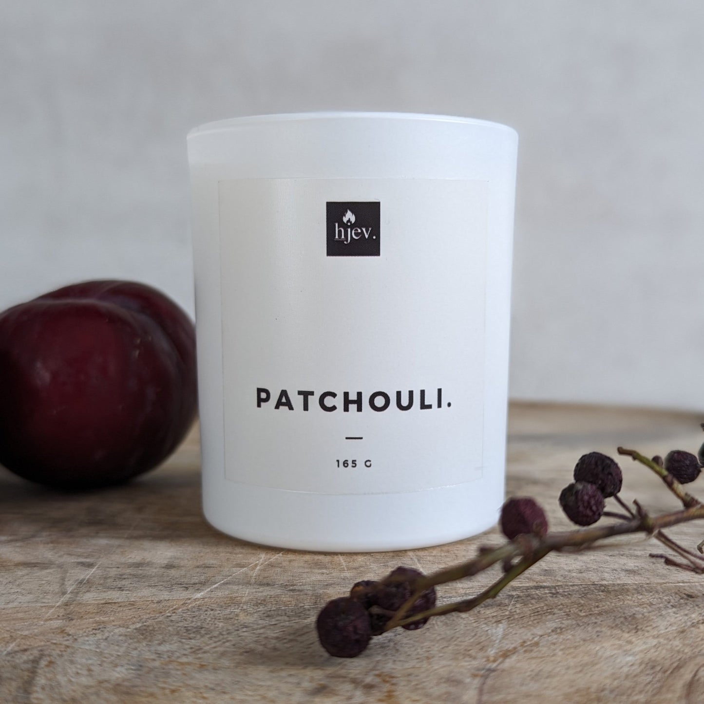 Een close-upafbeelding van de Patchouli en Pruim geurkaars van HJEV, gepresenteerd in een stijlvolle en luxueuze verpakking. De kaars verspreidt een warme en weelderige geur, waarbij de aardse tonen van patchouli harmoniëren met de zoete en sappige aroma's van pruim, waardoor een ontspannende en luxe sfeer in huis wordt gecreëerd.