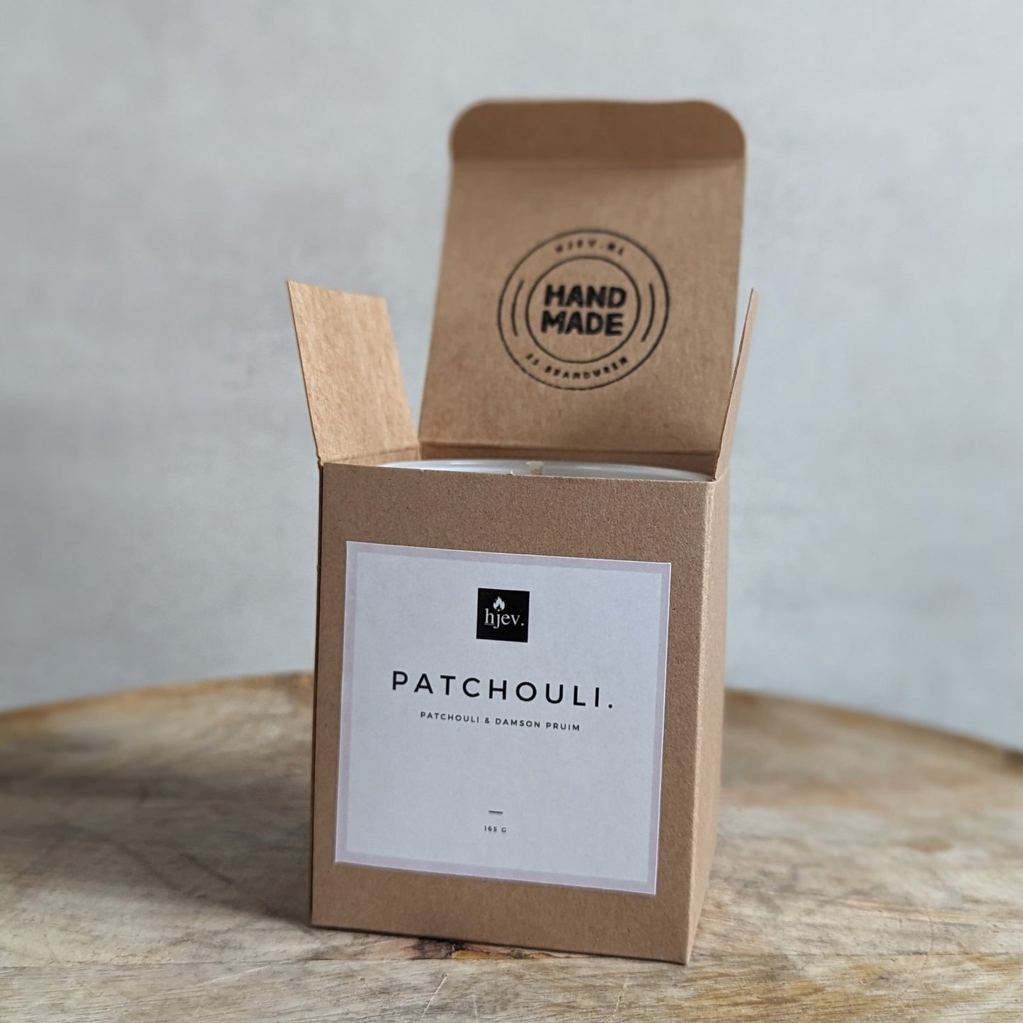 Een close-upafbeelding van de Patchouli en Pruim geurkaars van HJEV, gepresenteerd in een stijlvolle en luxueuze verpakking. De kaars verspreidt een warme en weelderige geur, waarbij de aardse tonen van patchouli harmoniëren met de zoete en sappige aroma's van pruim, waardoor een ontspannende en luxe sfeer in huis wordt gecreëerd.